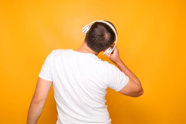 Kafasında beyaz kulaklık olan beyaz tişörtlü bir adam arkasında duruyor..