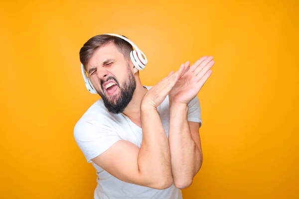 bearded man with white musical headphones listens to music and sings at the same time.