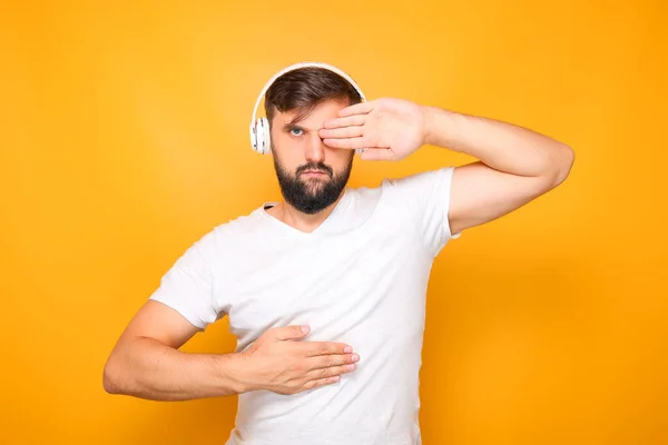 a man with a beard in white headphones, closes his eyes with his palms.