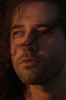 Bigudileri ve saçı yana bakan yakışıklı, açık renk gözlü bir adam. Güzel bir gün batımının yüzünde yumuşak, sıcak bir ışıkla izole edilmiş bir portre.