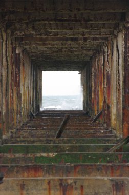 İskele içeriden çekilmiş. Arkasında deniz dalgaları olan kare mimariyi gösteriyor.