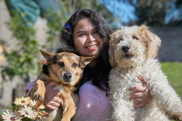 Latin kız parkta iki köpeğe sarılıyor. Köpeklerden biri Tilki Teriyeri 'nin soyundan ve diğeri de kunduzla kapkara. Güneşli bir bahar gününün tadını çıkarıyorlar..  