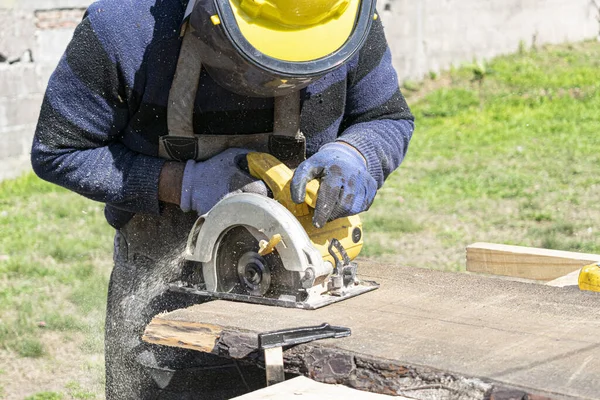 Man cutting wood with an electric saw.He wears a yellow protective helmet