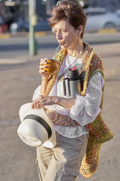 Olgun bir kadın güneşli bir şehir ortamında yerba eşi içiyor, bohem, zanaatkar tarzda ve düşünceli bir tavırla. Latin Amerika kimliğini ve geleneğini kutlayan günlük bir sahne..