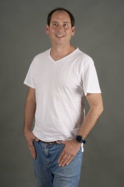 Kel bir adamın portresi, elleri kalçasında, gri bir arka planda. Beyaz tişörtlü, rahat ve kendinden emin bir tarz. Ticari kullanım için temiz ve çok yönlü resim.
