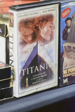 Diğer video kasetler arasında gösterilen orijinal Titanik VHS kaseti, klasik bir film ve 20. yüzyılın sonlarında ev eğlencesi ile ilişkili fiziksel bir formatı temsil ediyor..