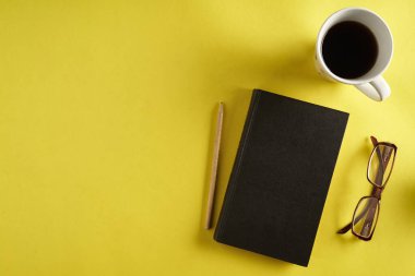 Sarı yüzey üst görünüm, kalem, siyah defter ve bir fincan kahve ile masa