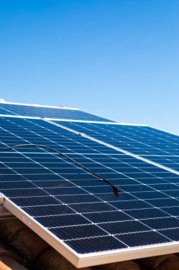 Güneş panelleri açık mavi bir gökyüzünün altında fayanslı bir çatıya monte edilir. Kurulumda konut kullanımı için çevre dostu enerji üretimi sergileniyor.