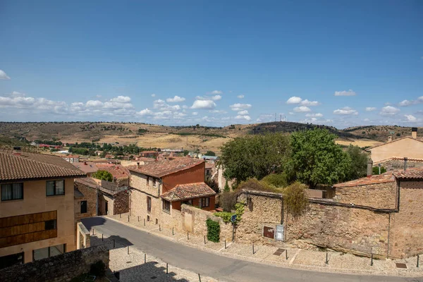 Sakin, dar bir cadde taştan binalar ve renkli bayraklarla kaplı küçük bir İspanyol köyünden geçiyor. Mavi gökyüzü konumun huzurlu atmosferine eklenir..