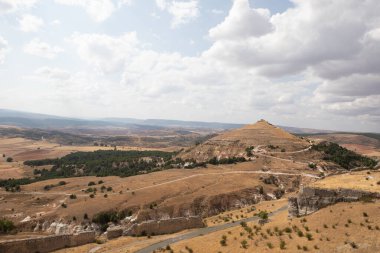 İspanya, Atienza, Guadalajara 'yı çevreleyen kayan tepelerin manzarası, açık hava keşfi ve fotoğrafçılık için mükemmel, parlak bir gökyüzü altında antik kalıntıları ve çimenli araziyi gösteriyor..
