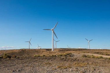 Rüzgâr türbinleri, kuru çimenler ve kayalık arazilerle çevrili sakin bir arazide uzun süre ayakta kalırlar. Ayar doğal ortamda yenilenebilir enerjinin güzelliğini gösteriyor..