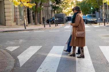 Huzurlu bir şehir ortamında, iki arkadaş bir zebra geçidinde yan yana yürür. Güneş ışığı ağaçların arasından süzülüyor, şık kıyafetlerini ve neşeli ifadelerini aydınlatıyor..