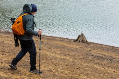 Yalnız bir gezgin sakin bir gölün kumlu kıyısında yürüyor. Bir tripod ve kamera ile donatılmış halde, alacakaranlıkta suyun yüzeyine yerleşen dingin güzelliği yakalar..