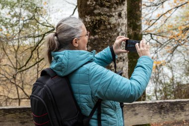 Deniz mavisi ceketli bir kadının akıllı telefonuyla nefes kesici manzarayı yakalaması biraz zaman alır. Huzurlu göl manzarasının tadını çıkarırken etrafını renkli sonbahar yaprakları sarıyor..
