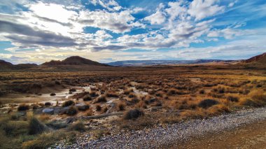Altın otlar uzak dağlarla çevrili sakin bir çöl vadisinde uzanıyor. Akşam yaklaşırken, gökyüzü dönen bulutlar ve yumuşak güneş ışığıyla barışçıl bir atmosfer yaratıyor..