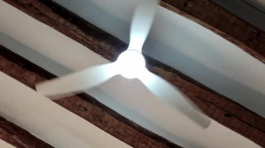 Bir tavan vantilatörü zarif bir şekilde döner, yukarıdaki ahşap kirişlerin güzelliğini gösterirken yumuşak bir ışık saçar. Sakin atmosfer, rahat bir iç mekanda rahatlamaya davetiye çıkarır..