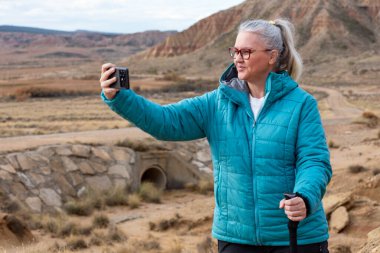 Bir kadın, Bardenas Reales 'te sakin bir anın tadını çıkarıyor. Telefonuyla muhteşem çöl manzarasının ortasında selfie çekiyor. Eşsiz kaya oluşumları macerası için mükemmel bir zemin oluşturuyor..