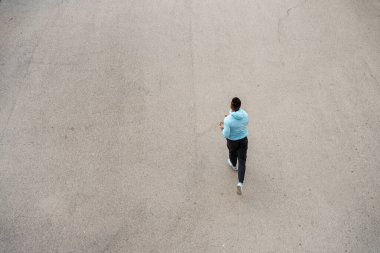 Açık mavi bluzlu yalnız bir koşucu boş bir cadde boyunca koşar. Öğleden sonra güneşi yumuşak gölgeler bırakır, sakin bir atmosfer yaratır koşmak için mükemmel.