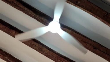 Bir tavan vantilatörü zarif bir şekilde döner, yukarıdaki ahşap kirişlerin güzelliğini gösterirken yumuşak bir ışık saçar. Sakin atmosfer, rahat bir iç mekanda rahatlamaya davetiye çıkarır..