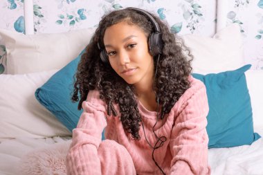 Çiçek desenleriyle süslenmiş rahat bir odada güzel kıvırcık saçlı genç bir kız kulaklıklarıyla müzik dinliyor. Rahatlamış ve memnun görünüyor, ezgilerine dalmış..