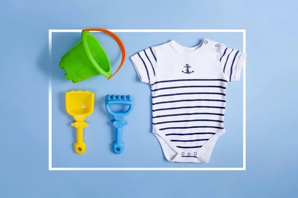 top view of framed baby sailor clothes, bucket, shovel and beach rake with blue background. Summer concept.