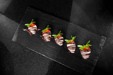 5 çileğin üst görüntüsü mermer üzerine siyah bir levha üzerine dizilmiş.