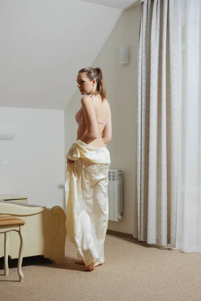 Bonita joven en el dormitorio quitándose peignoir de seda cerca de la cama — Foto de Stock