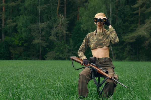 Atractiva chica cazadora con carabina de caza mirando en binocul — Foto de Stock