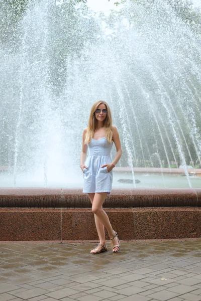 Menina atraente em vestido azul curto fica na frente da fonte — Fotografia de Stock