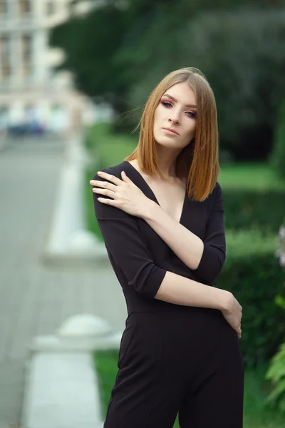 Elegante modelo de moda jovem em preto em geral com profundo decotado no parque da cidade — Fotografia de Stock