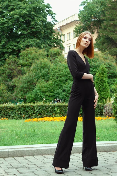 Stylish young fashion model in black overall with deep decollete in city park — Stock Photo, Image
