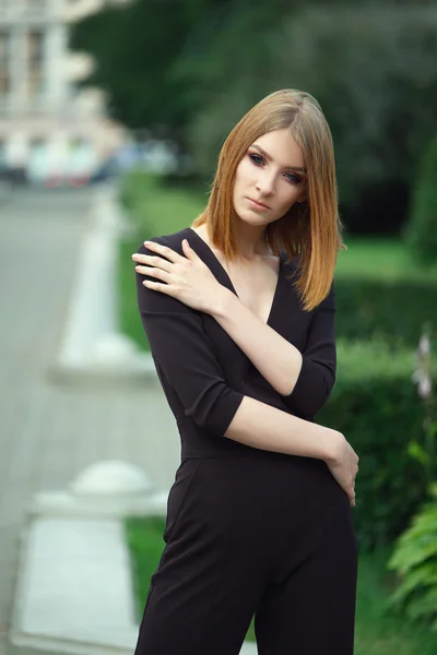 Elegante modelo de moda jovem em preto em geral com profundo decotado no parque da cidade — Fotografia de Stock