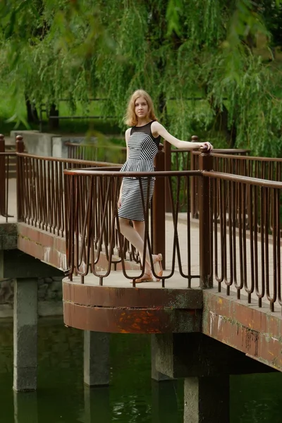 Muito jovem adolescente em vestido listrado em uma ponte — Fotografia de Stock