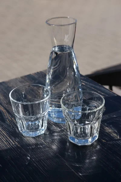 Zwei Gläser und eine Wasserflasche auf einem schwarzen Holztisch eines Cafés — Stockfoto