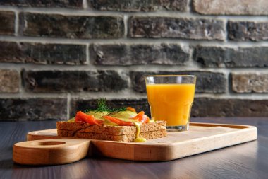 Somonlu sandviç, erimiş peynir, baharatlı sos ve bir bardak portakal suyu.