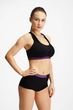 Siyah spor kıyafetli genç bir kadın beyaz arka planda poz veriyor.