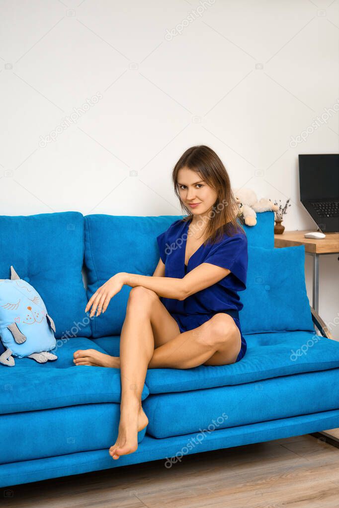 Pretty young woman sits on blue sofa at home