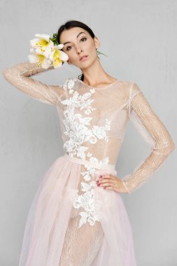 Şeffaf tül elbiseli, dantelli, elinde çiçeklerle poz veren güzel bir kadın.