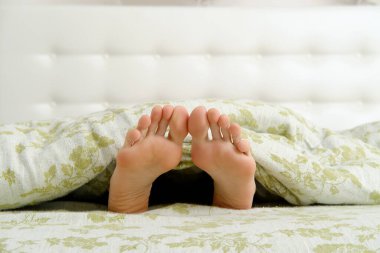 Battaniyenin altından sarkan uzun ayak parmakları olan çıplak kadın ayakları.