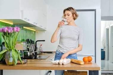 Güzel, genç bir kadın, mutfakta kahvaltı yapmadan önce su içer.