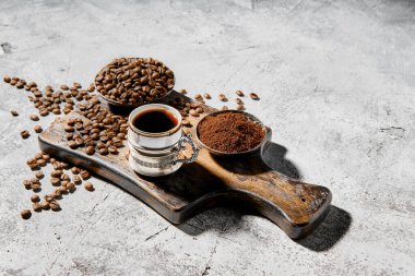 Sıcak bir fincan espresso, tahtanın üzerine dağılmış kahve çekirdekleri ve sabah güneşinin altında bir demlik.