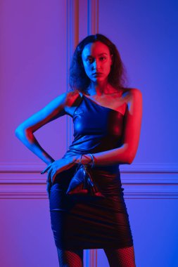 Neon ışıklarının altında küçük el çantasıyla poz veren Afro-Amerikan modeli.