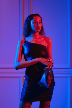 Zarif Afro-Amerikan modeli neon ışıkların altında üçgen el çantasıyla poz veriyor.