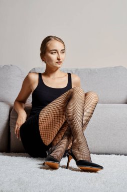 Calm young woman sits on the carpet leaning to the sofa