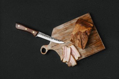 Tütsülenmiş domuz pastırması, kahverengi ekmek ve yumurtalar ahşap kesim tahtasında.