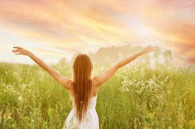 Young woman spreading hands to the sides and facing to the sun in the field