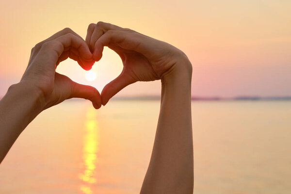 Female palms form the shape of the heart with sunset on background