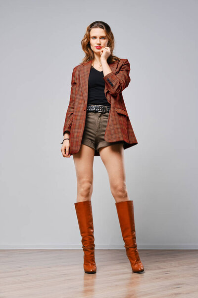 Полная фотография красивой женщины в коричневой клетчатой куртке и сапогах