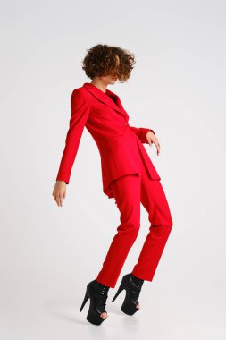 Kırmızı pantsui ve direk dans botları giymiş zarif bir kadın, kavisli ve parmak ucunda duruyor.