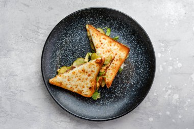 Biftek, salatalık turşusu ve üçgen parçalı peynirli sandviç manzarası.